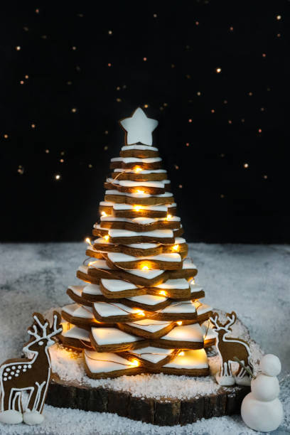 木製のケーキスタンドに白い王室のアイシングをあしらった積み重ねられたジンジャーブレッドスタークッキーのイメージクリスマスツリーは、照らされた妖精の光、トナカイのビスケット� - star shape christmas ornament heap stack ストックフォトと画像