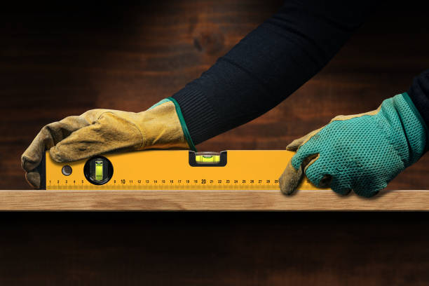Manual Worker Holding an Orange Spirit Level on a Wooden Plank Manual worker with protective work gloves, holding an orange construction spirit level, on top of a wooden plank. spirit level stock pictures, royalty-free photos & images