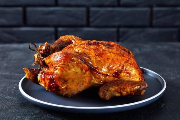 istock Whole roast chicken on a plate in front of black brick wall on a dark grey concrete table, close-up 1356938841