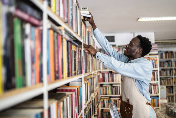 libraio che organizza i libri in uno scaffale - service occupation candid small business carrying foto e immagini stock