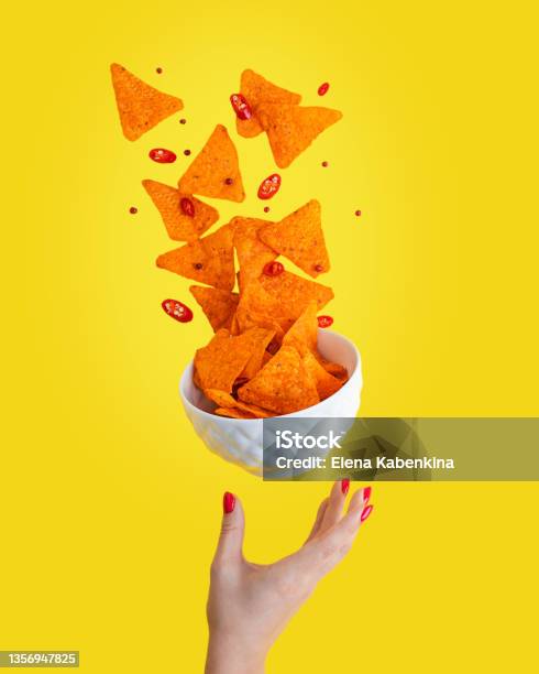 Levitation Of Hot Nachos Mexican Crispy Fried Tortilla Chips With Chili Pepper Slices Served In White Bowl With Woman Palm Against Yellow Background Stock Photo - Download Image Now