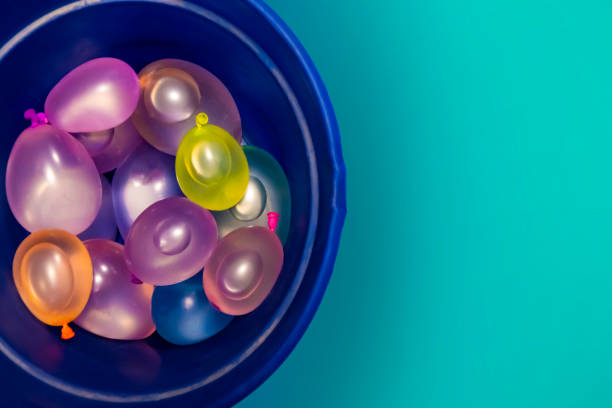A bucket full of fun: Water balloons waiting for the game Pastel-colored latex water balloons are piled up in a blue bucket ready for a water balloon fight. There is copy space to the right of the image. water balloon stock pictures, royalty-free photos & images