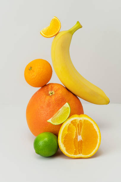 istock Fresh grapefruit, banana, cut in half orange, tangerine, lime slice on light grey background. Healthy food with vitamins. Ripe juicy fruits balanced on each other. Vegetarian snack. Trendy still life 1356954331
