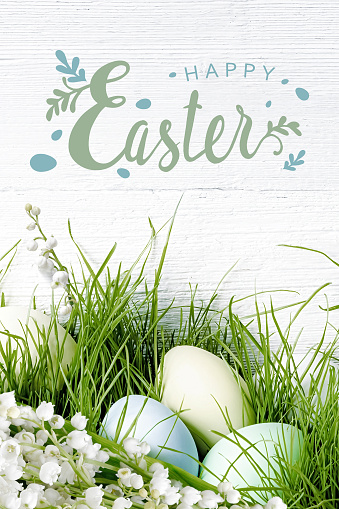 Easter holiday card with lettering. Easter eggs laying in green grass with lilies of the valley flowers.
