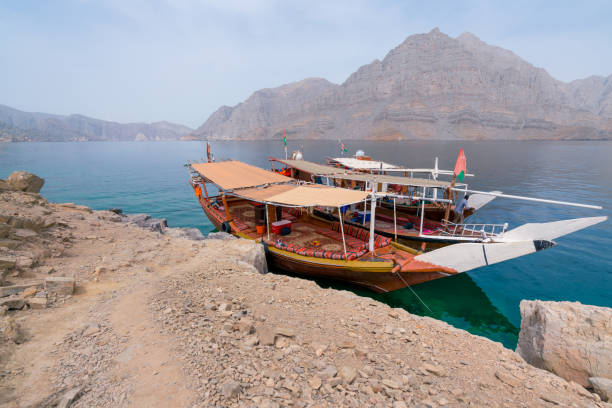 Two traditional Arabian dhow boats parked by an island in turquoise fjords of Musandam, Oman. Hot, hazy day in fjords of Arabia. stock photo