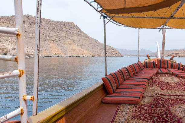 View from the traditional Arabian dhow boat sailing on the sea. Red pillows and carpets, yellow fabric shade. Sailing in fjords of Arabia in Musandam, Oman. stock photo