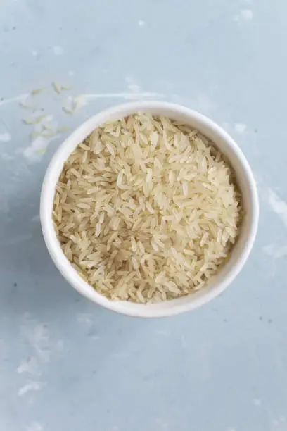 Photo of White milled long grain rice in a white bowl on a gray background. Vegetarian food concept. Vertical orientation. Rice dishes are cooked in all countries of the world. Popular cereal. Top view.