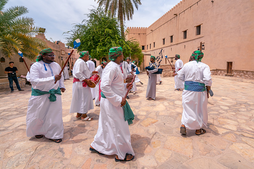 Nizwa, Oman - 04.06.2018: Men in traditional dress playing pipes, singing and dancing around in a ceremony. Event in medieval arabian fort of Nizwa, Oman. Middle east festival.