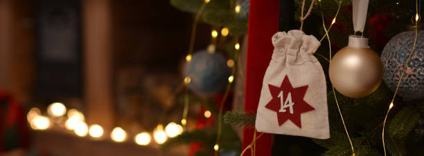 antecedentes navideños. calendario de adviento en forma de bolsas ecológicas cuelga en el árbol de navidad en el fondo de la sala de navidad con una chimenea de madera - advent calendar christmas number number 14 fotografías e imágenes de stock