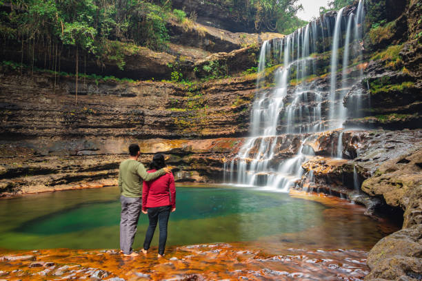 istock couple standing near waterfall flowing streams falling from mountain at morning from flat angle 1356961231