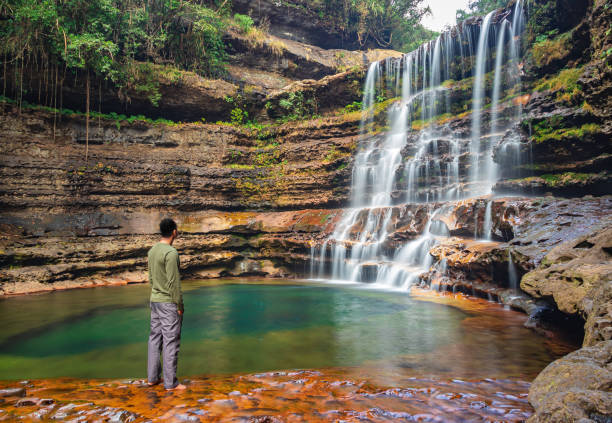 istock young man standing near waterfall flowing streams falling from mountain at morning from flat angle 1356961421