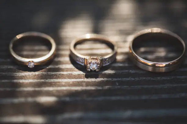 Photo of Three rings on wooden background. Engagement ring and two wedding bands on wooden table. White gold wedding jewelry.