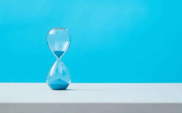 Hourglass with blue sand on the table.