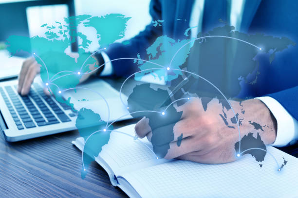 istock Wholesale and logistics concept. Man using laptop in office, world map illustration on foreground 1356969232