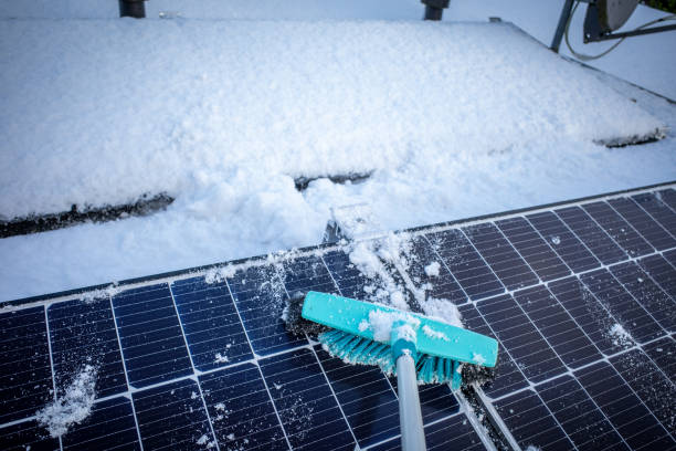 solar panels of a photovoltaic system on a roof are cleared of snow with a broom - solar panels of a photovoltaic system on a roof are cleared of snow with a broom stockfoto's en -beelden