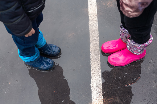 Two children wearing red rain boots jumping into a puddle. Close up. Kids having fun with splashing with water.