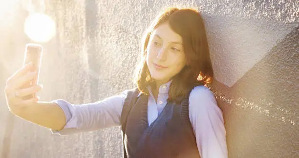 Photo of Female teenager shooting a selfie at sunset with lens flare
