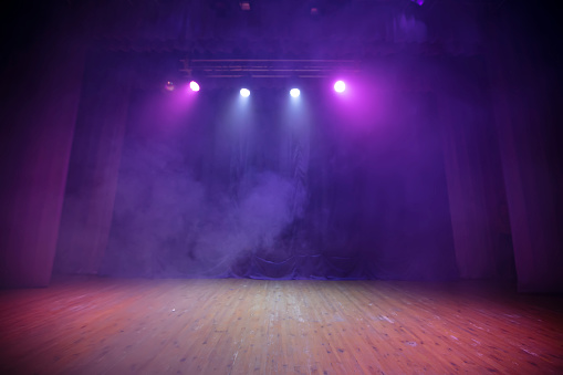 A stage for performances with purple curtains, wood floor and all in smoke. Theatrical background.