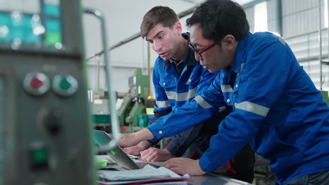 Multiracial Group of Techician male Engineers in uniform are consulting at a CNC machine for better production process both are agree to adjust condition and indicator for operating machinery manufacturing in Automobile Industry.