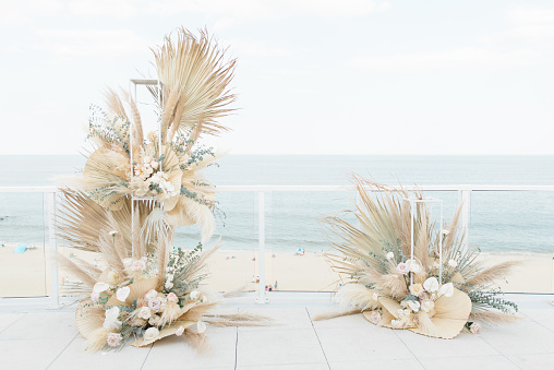A beautiful bohemian natural dried floral wedding arch on a balcony overlooking a beach.