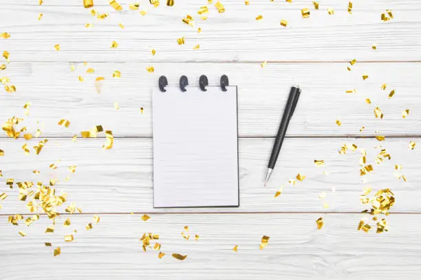 Festivedecorations and notebook with wish list on white rustic table, flat lay style. Planning concept.