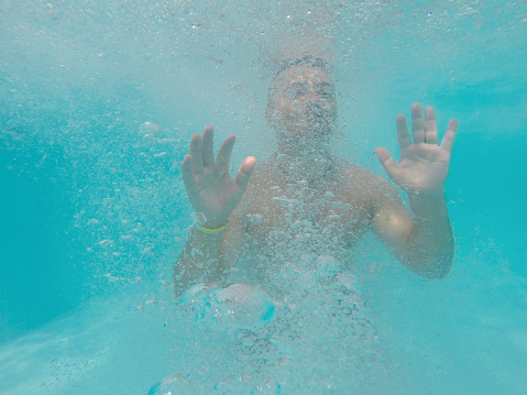 Young man drowning underwater into sea or ocean, blue water with bubbles