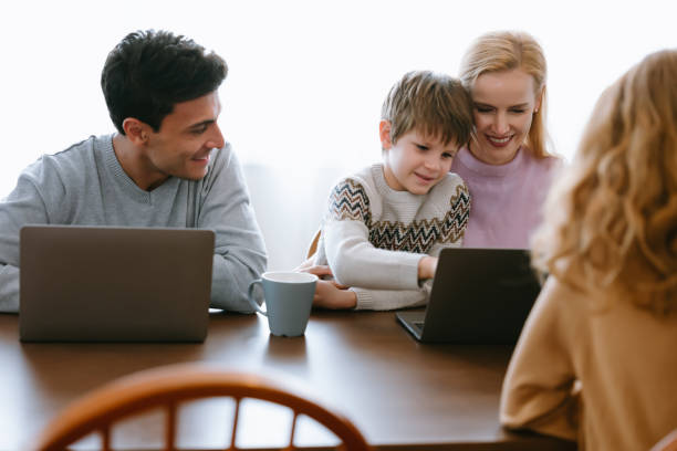 istock Cheerful family parents and kids are having fun together using  laptop computer sit on table in kitchen at home on winter day. Enjoying spending time together. 1356982229