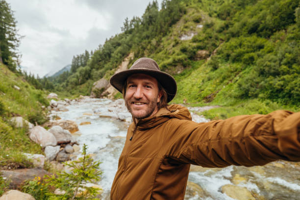istock Young man on a hike takes selfie by the river 1356983626