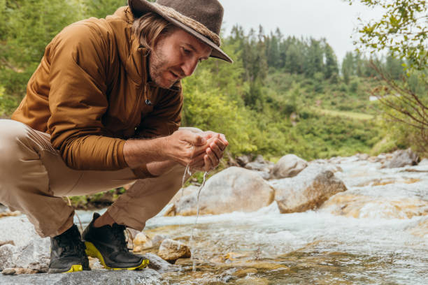 istock Young man hand cupping water from river, man on a hike stops to refresh by the river 1356985314