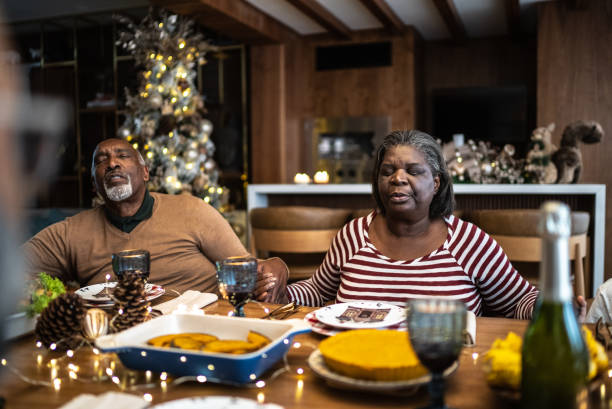 Senior couple praying with family on Christmas lunch or dinner at home