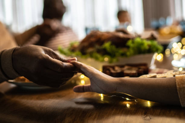 Hands of family members praying before lunch or dinner at home