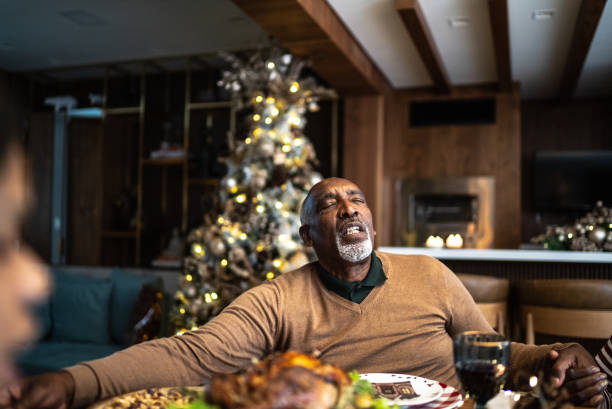 Senior man praying with family on Christmas lunch or dinner at home
