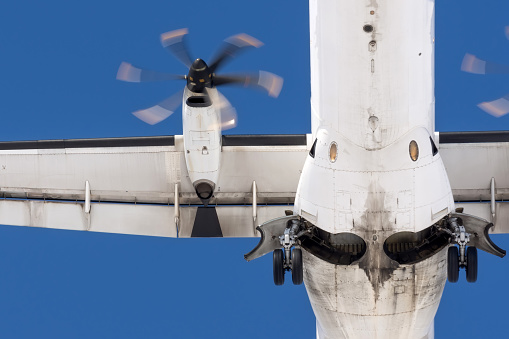 Turboprop aircraft flies overhead, view of the landing gear, wing and engine