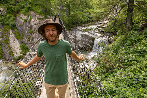 Young man on a hike walks on a suspended bridge on the forest. People weekend activity