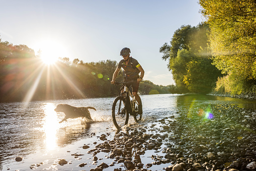 Male athlete crossing river with bicycle and his dog