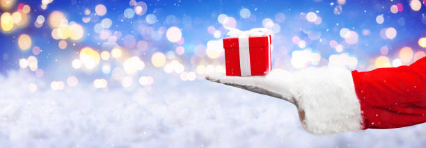 istock Santa Claus hand holding a wrapped Christmas present. 1356999426
