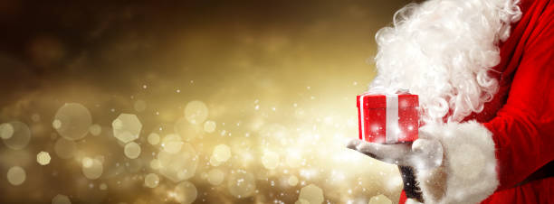 istock Santa Claus hand holding a wrapped Christmas present. 1356999449