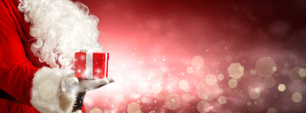 istock Santa Claus hand holding a wrapped Christmas present. 1356999477