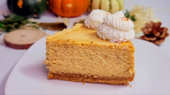 Slice of pumpkin cheesecake with whipped cream on a white serving plate