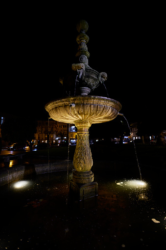 Verín town square, illuminated ornamental fountain, Verín town, Ourense province, Galicia, Spain. Monterrei defensive towers illuminated on the background mountain.