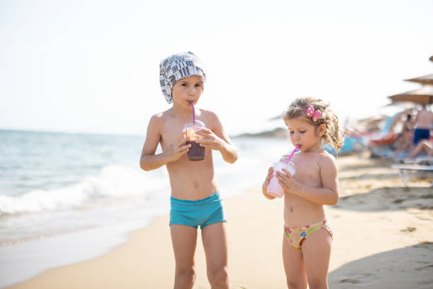 istock Brother and sister spending time on beach while they drink milkshake 1357002065