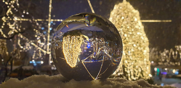 glass ball with snowflakes illuminated by colorful light of christmas garland.