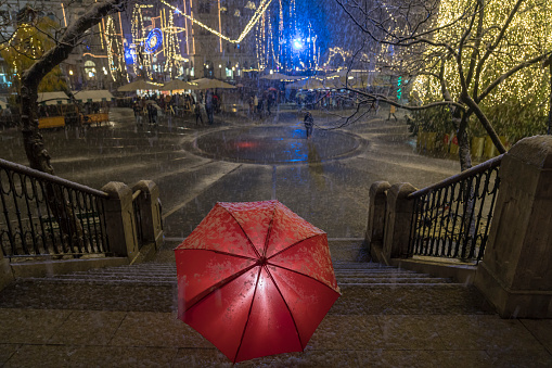 People gathering on Presern trg at night and enjoying snow and Christmas tree with beautiful decorations. In front view illuminated red umbrella