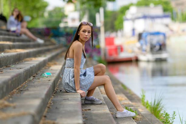 A portrait of a pretty young woman taken in the summertime in a city sitting on a staircase next to a river.