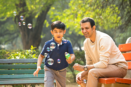 Carefree father and son having fun playing with bubble gun at park