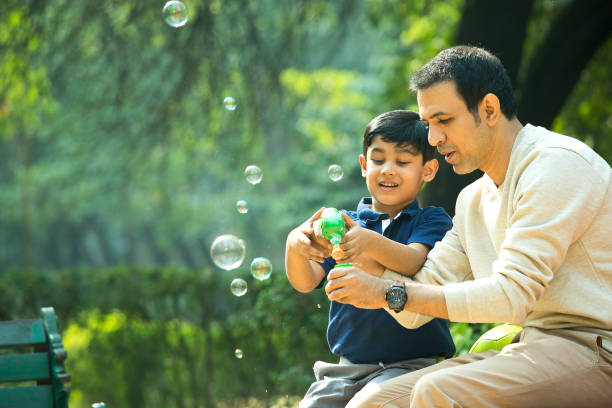 padre e hijo jugando con una pistola de burbujas en el parque - bubble wand bubble child playful fotografías e imágenes de stock