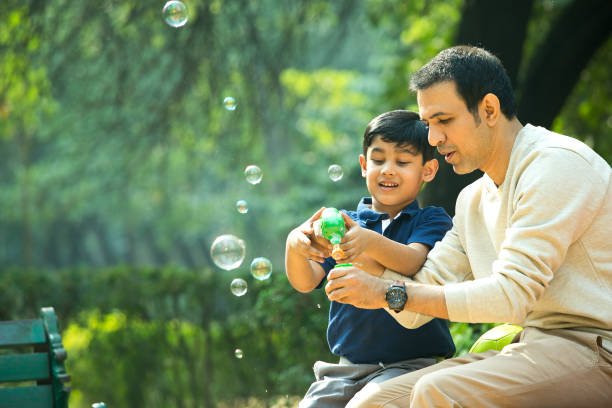Father and son playing with bubble gun at park stock photo