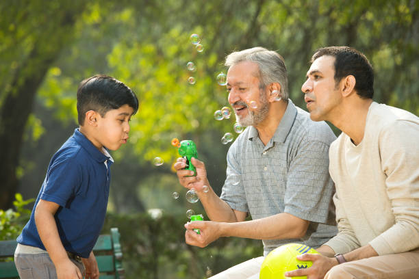 istock Senior man blowing bubbles with son and grandson at park 1357005054