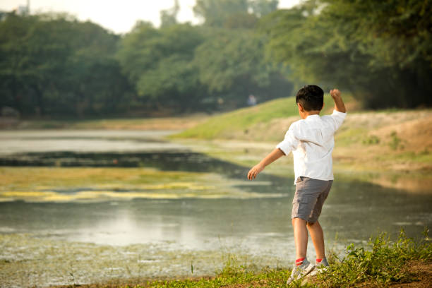 istock Rear view of boy standing at riverbank while exploring nature 1357007872