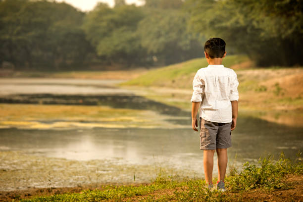 Rear view of boy standing at riverbank while exploring nature